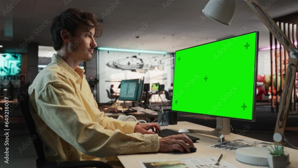 Portrait of Creative Caucasian Man Sitting at a Desk Using Desktop Computer with Mock-up Green Screen Chromakey. Male Concept Artist Working in Game Design Startup Office, Creating Immersive Gameplay. Portrait of Creative Caucasian Man Sitting at a Desk Using Desktop Computer with Mock-up Green Screen Chromakey. Male Concept Artist Working in Game Design Startup Office, Creating Immersive Gameplay.