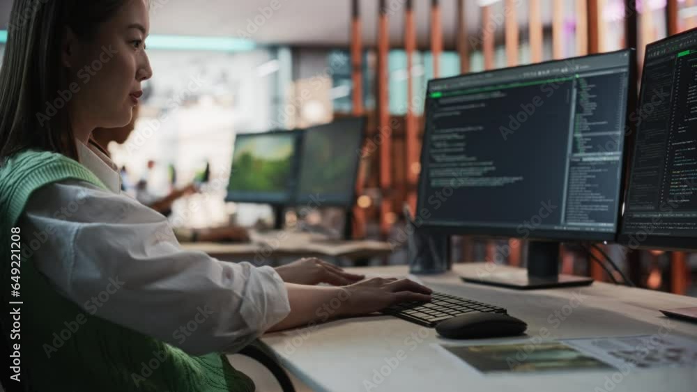 Female Asian Game Programmer Coding On Desktop Computer In Game Development Studio Diverse Office. Focused Woman Writes Lines Of Code, Does AI Engineering For New Immersive 3D Survival Video Game. Female Asian Game Programmer Coding On Desktop Computer In Game Development Studio Diverse Office. Focused Woman Writes Lines Of Code, Does AI Engineering For New Immersive 3D Survival Video Game.