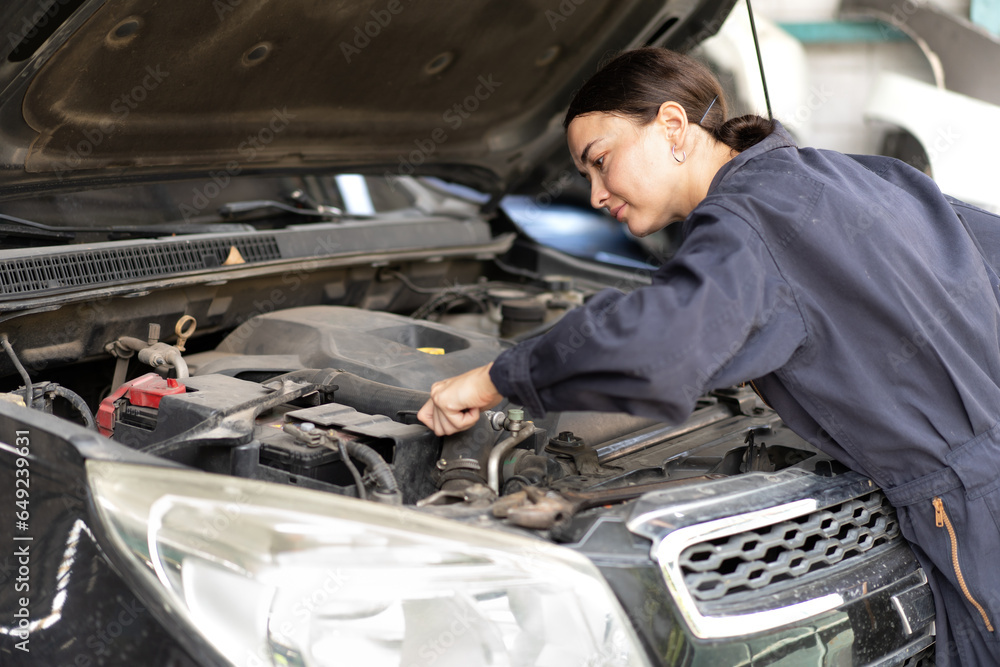 Auto mechanic working in vehicle repair service garage. Long hair woman inspecting breaking automobile engine, motor parts breakdown, examining oil. People in automotive maintenance business concept Auto mechanic working in vehicle repair service garage. Long hair woman inspecting breaking automobile engine, motor parts breakdown, examining oil. People in automotive maintenance business concept