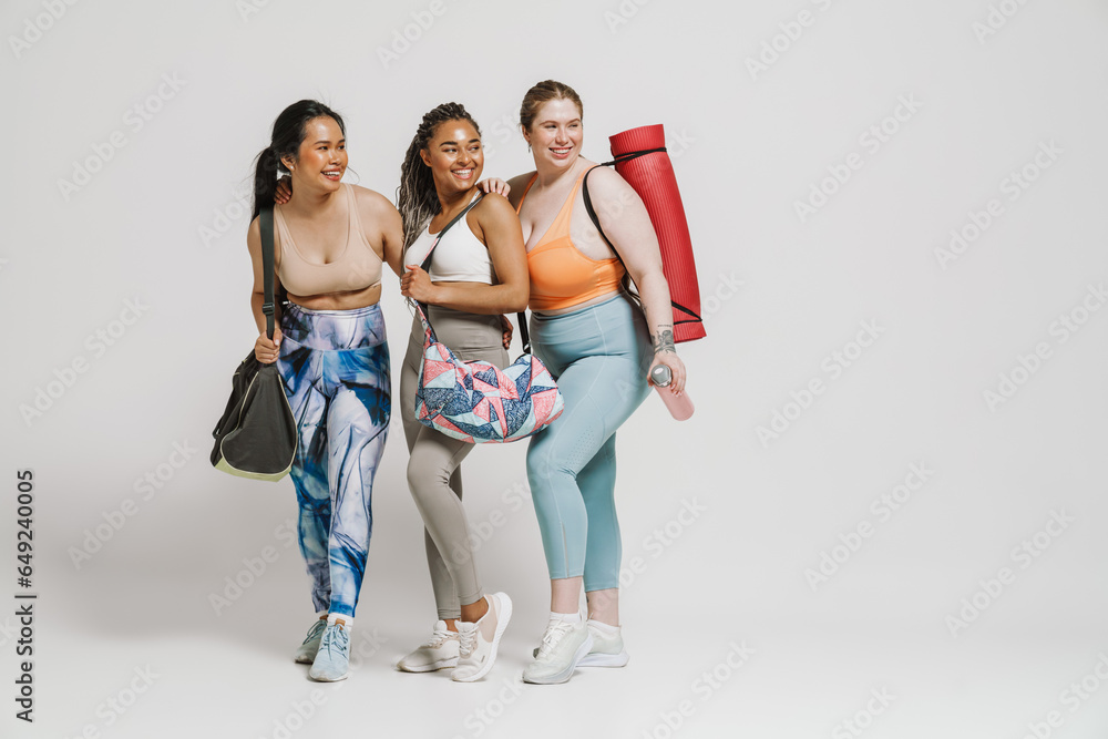 Obraz premium Three cheerful women with yoga mat posing isolated over white background