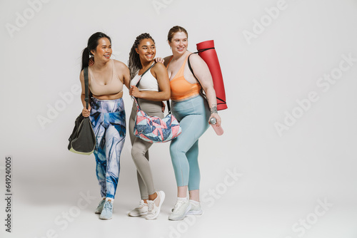 Three cheerful women with yoga mat posing isolated over white background