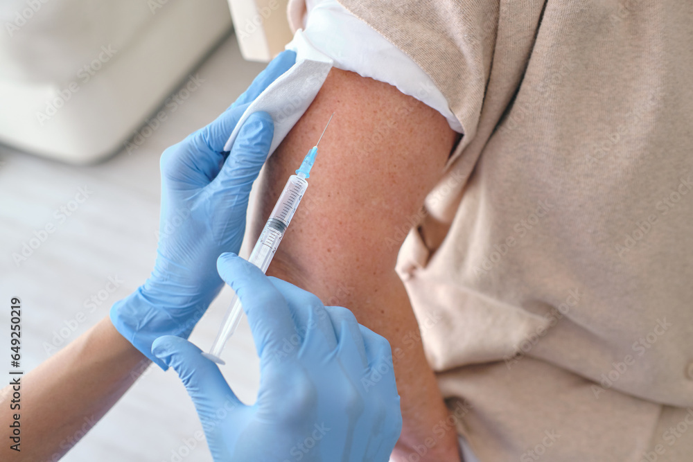 Crop nurse in sterile gloves vaccinating patient with syringe Crop nurse in sterile gloves vaccinating patient with syringe