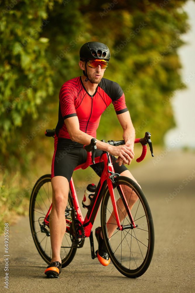 Professional triathlete training outdoors, wearing sportswear and helmet, riding bike along the road. Concept of professional sport, triathlon preparation, competition, athleticism