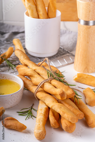 Italian Mediterranean grissini bread sticks, with aromatic oil and sprigs of rosemary, on a white kitchen table background photo