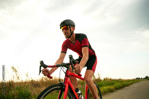 Dynamic image of motivated sportsman, athlete riding bicycle along the road, training outdoors. Concept of professional sport, triathlon preparation, competition, athleticism photo