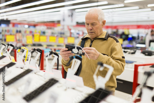 Elderly man buys a modern digital tablet in the showroom of the store