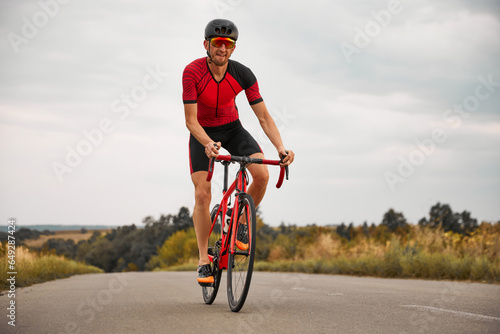 Competitive sportsman, triathlete riding bicycle on road outdoors, training for marathon. Concept of professional sport, triathlon preparation, competition, athleticism photo