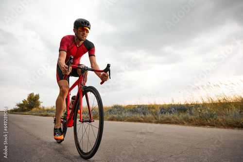 Competitive and motivated man, triathlete riding bicycle on road outdoors, training for marathon. Concept of professional sport, triathlon preparation, competition, athleticism