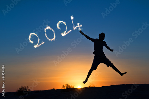 2024 written with sparkles, silhouette of a boy jumping in the sun, new year card
