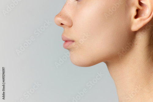 Cropped side view image of female face isolated over grey studio background. Reduction of double chin