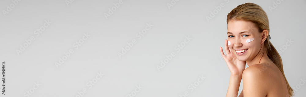Portrait of pretty, smiling, young girl with well-kept skin with face cream isolated over grey studio background Portrait of pretty, smiling, young girl with well-kept skin with face cream isolated over grey studio background