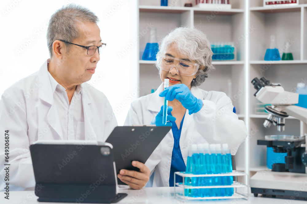 Senior scientists analyzing pharmaceuticals, asian people, senior man and woman, experienced experts in science, conducting pharmaceutical research in modern lab setting with powerful microscope. Senior scientists analyzing pharmaceuticals, asian people, senior man and woman, experienced experts in science, conducting pharmaceutical research in modern lab setting with powerful microscope.