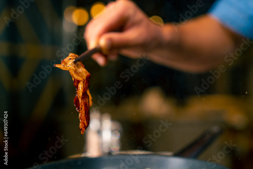 A close-up of a chef with tongs in his hand frying bacon for a burger in the professional kitchen of an Italian restaurant