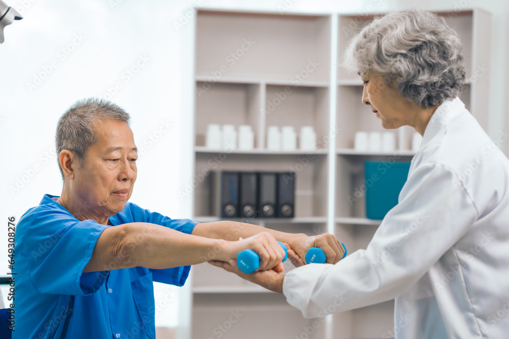 Asian people mature woman doctor giving male elderly patient through indoor physical therapy in a healthcare wheelchair, emphasizing hands-on support and recovery. expert physical therapy Asian people mature woman doctor giving male elderly patient through indoor physical therapy in a healthcare wheelchair, emphasizing hands-on support and recovery. expert physical therapy