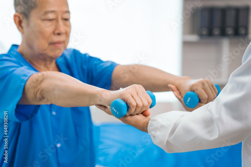 Asian people mature woman doctor giving male elderly patient through indoor physical therapy in a healthcare wheelchair, emphasizing hands-on support and recovery. expert physical therapy