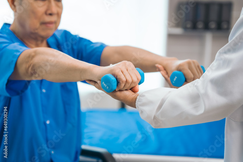 Asian people mature woman doctor giving male elderly patient through indoor physical therapy in a healthcare wheelchair  emphasizing hands-on support and recovery. expert physical therapy