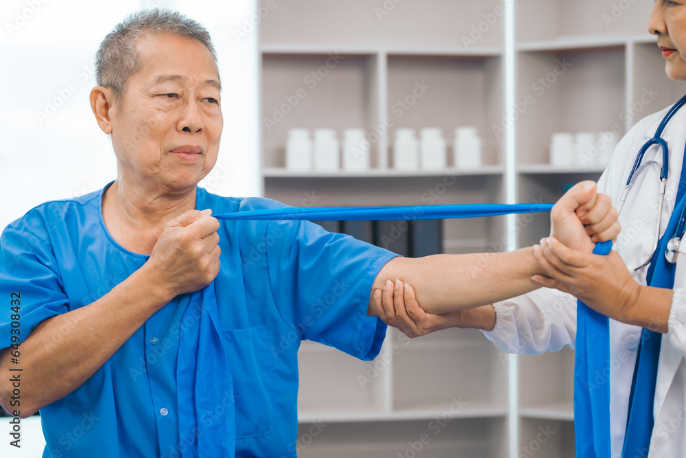 Obraz premium Asian people mature woman doctor giving male elderly patient through indoor physical therapy in a healthcare wheelchair, emphasizing hands-on support and recovery. expert physical therapy