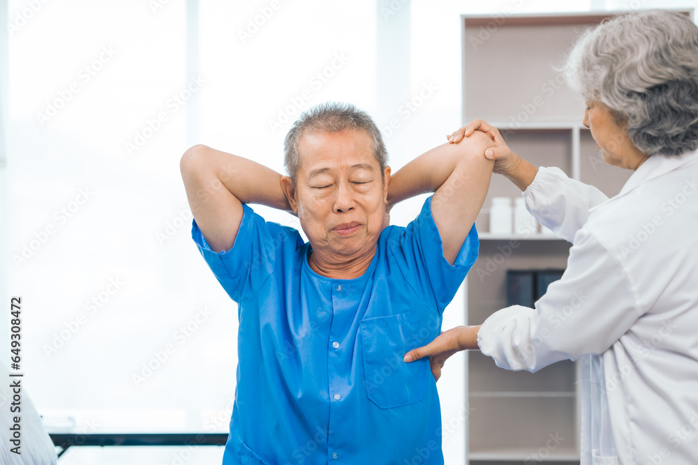 Obraz premium Asian people mature woman doctor giving male elderly patient through indoor physical therapy in a healthcare wheelchair, emphasizing hands-on support and recovery. expert physical therapy