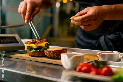 A close-up of a chef preparing a burger with beef patty with vegetables and cheese in the professional kitchen of an Italian restaurant