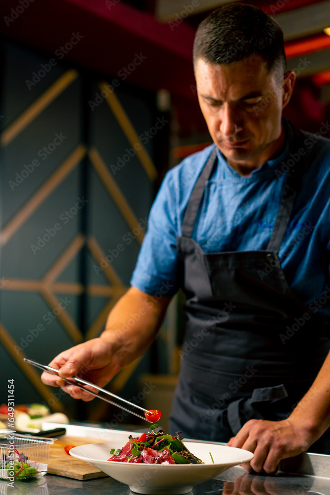 The chef of an Italian restaurant decorates a dish he has prepared in a professional kitchen 