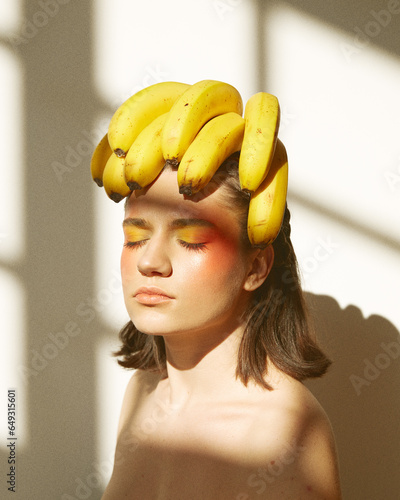 A sunlit fashion shoot featuring a naturally beautiful girl with bananas against a white backdrop, exuding fresh, healthy, and organic vibes. (ID: 649315601)