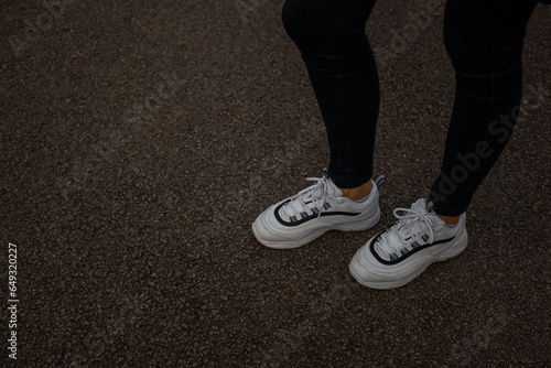 White sneakers on the feet of a girl in black jeans on the street