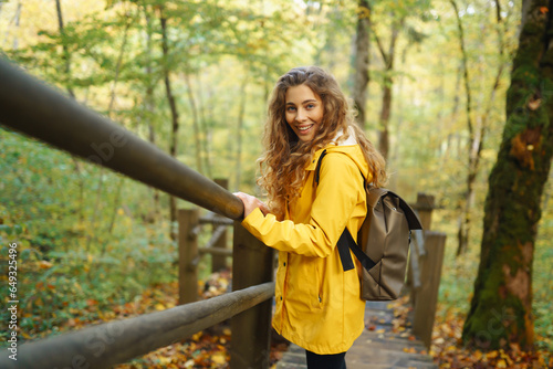 Active woman with backpack enjoys hiking on wooden stairs in autumn forest. A tourist female is engaged in mountaineering along a forest path, having fun, exploring nature.