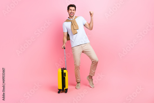 Full body photo of guy fist up hooray celebrate his victory free pass tickets traveler carry suitcase isolated on pink color background photo