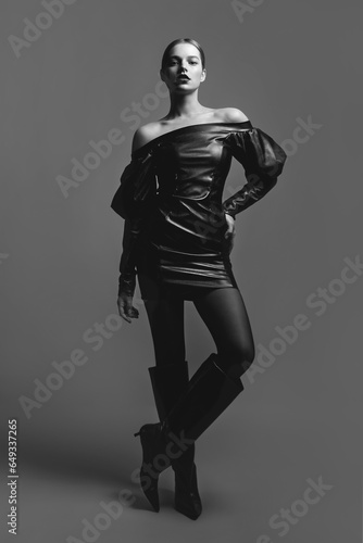 Beautiful young girl with bright lipstick in a black leather dress posing in the studio. Emphasis on the hands.