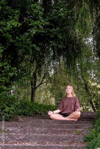 Woman meditates in nature outdoor.At ground level, a relaxed woman meditates and breathes while sitting in Lotus pose next to fragrant incense during a yoga class in the garden © shintartanya