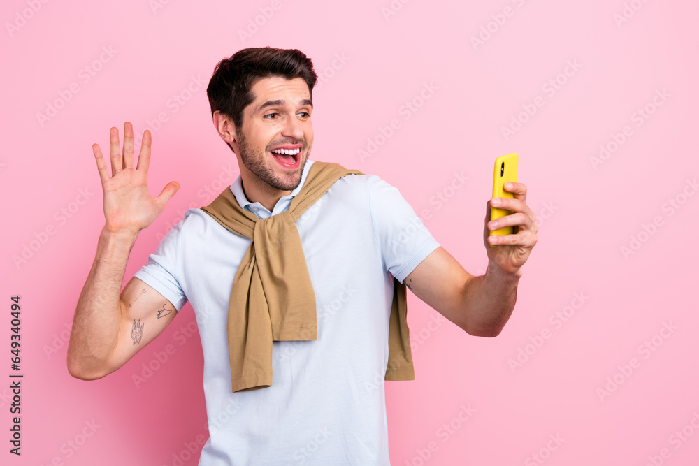 Portrait of positive overjoyed man hold smart phone make selfie video call arm palm waving hi isolated on pink color background Portrait of positive overjoyed man hold smart phone make selfie video call arm palm waving hi isolated on pink color background