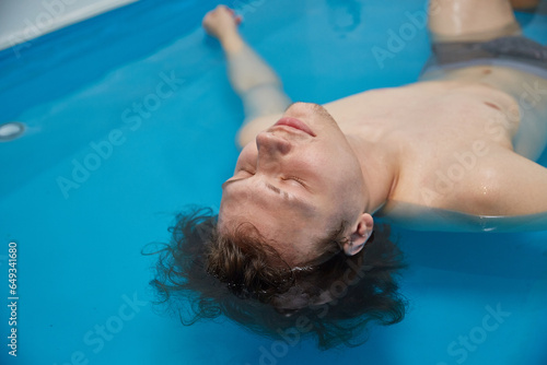 Handsome young man is swimming in the pool on his back. Relaxation and spa therapy. © Татьяна Кутина