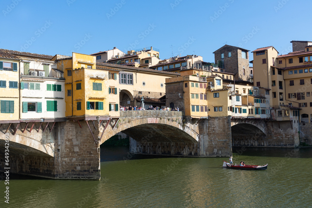 view of Arno river with tourist boat and ponte vecciho old bridge