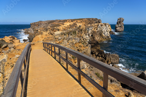 Wooden path in the Papoa island in the site of geological interest of the cliffs of the Peniche peninsula, portugal, in a sunny day with the rock formations. photo