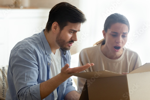 Angry man and woman annoyed by bad delivery service, unboxing parcel, looking into open cardboard box, dissatisfied customers received wrong or broken internet store order, complaint