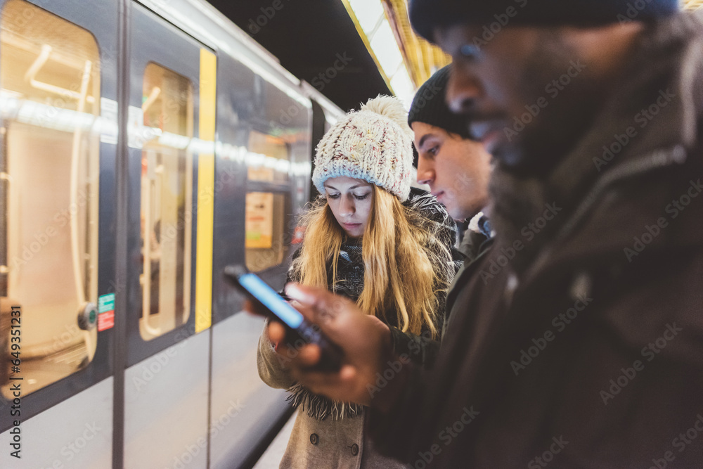 three young adult friends waiting metro and checking smartphone