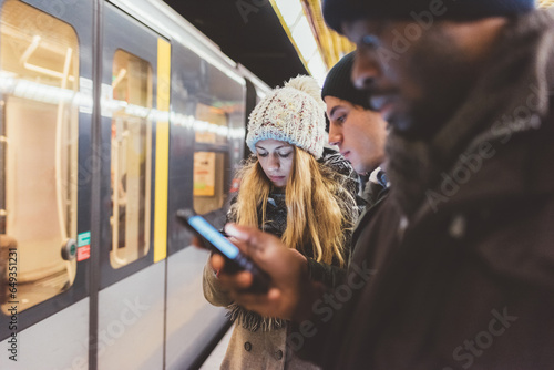 three young adult friends waiting metro and checking smartphone