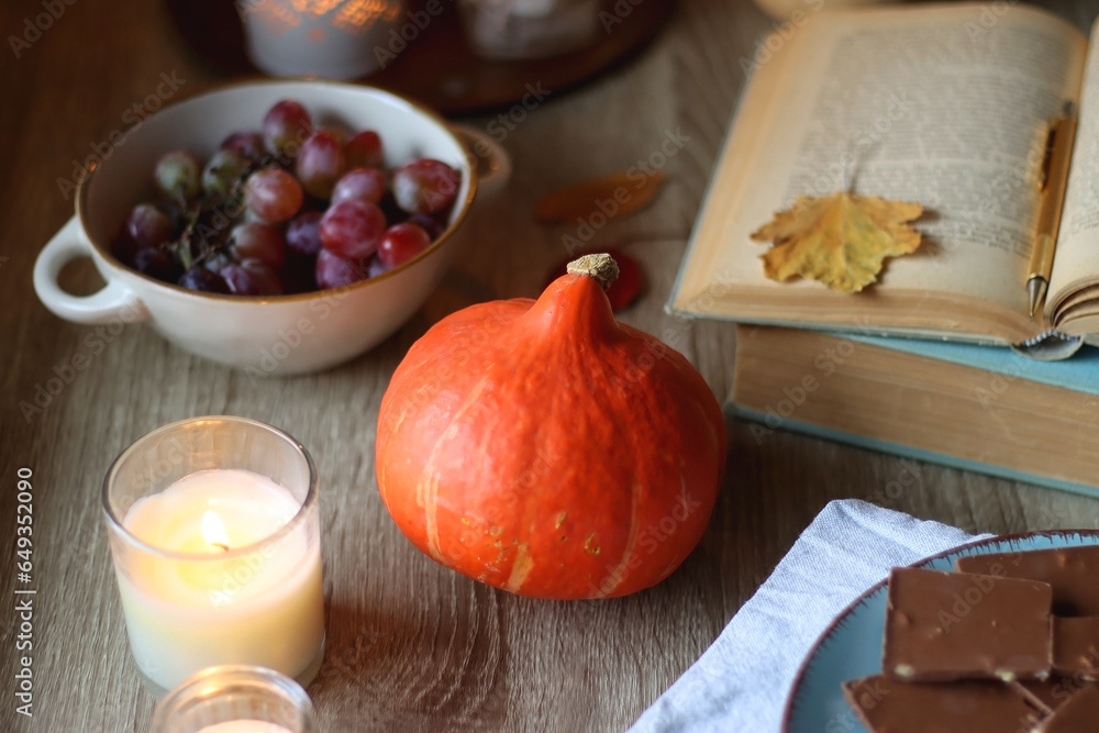 Cup of tea or coffee, plate with desserts, dried oranges, bowl of grapes, scented candles, vintage books, pumpkins and autumn leaves on the table. Autumnal hygge. Selective focus.