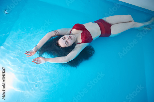 A young woman enjoys relaxing in a swimming pool or a bath with salt water. A brunette with loose hair is relaxing in a spa salon. Top view. Copy Space.