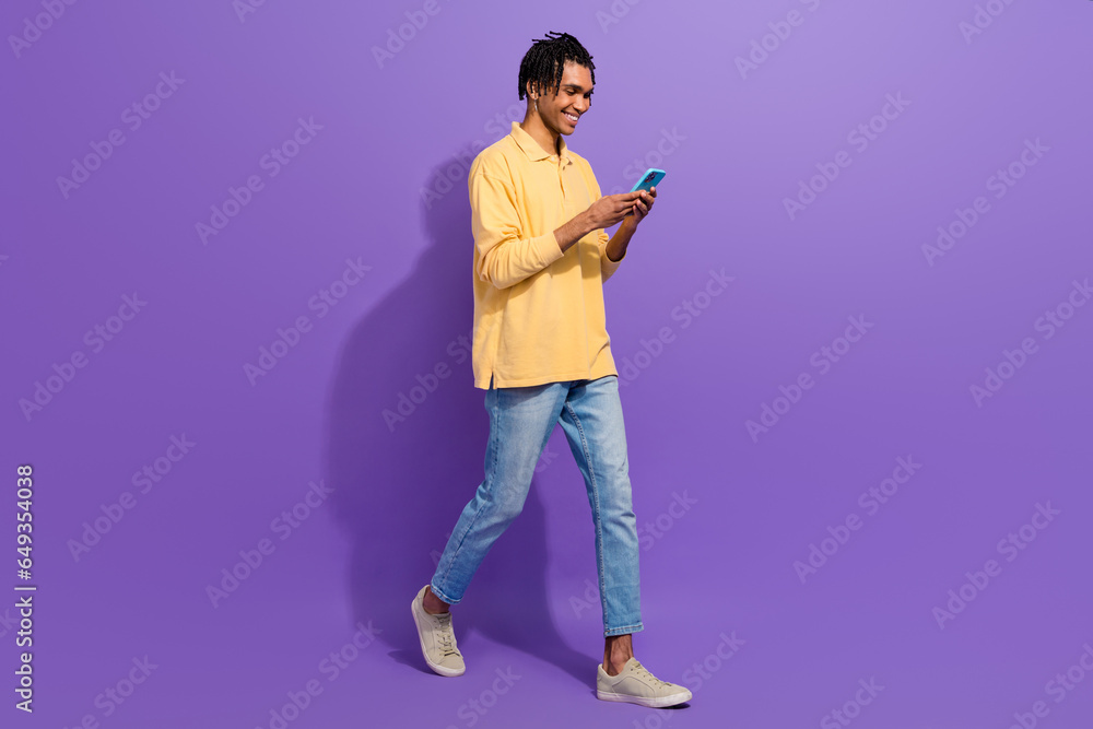 Full body size photo of funny young man steps smartphone telegram messenger internet web gadget isolated on purple color background Full body size photo of funny young man steps smartphone telegram messenger internet web gadget isolated on purple color background