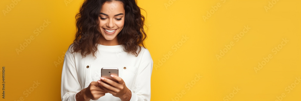 Latin woman wearing a white t-shirt and holding mobile phone looking at smartphone isolated on yellow background - obrazy, fototapety, plakaty 