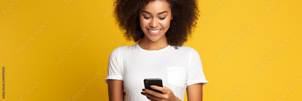 Latin woman wearing a white t-shirt and holding mobile phone looking at smartphone isolated on yellow background - obrazy, fototapety, plakaty 