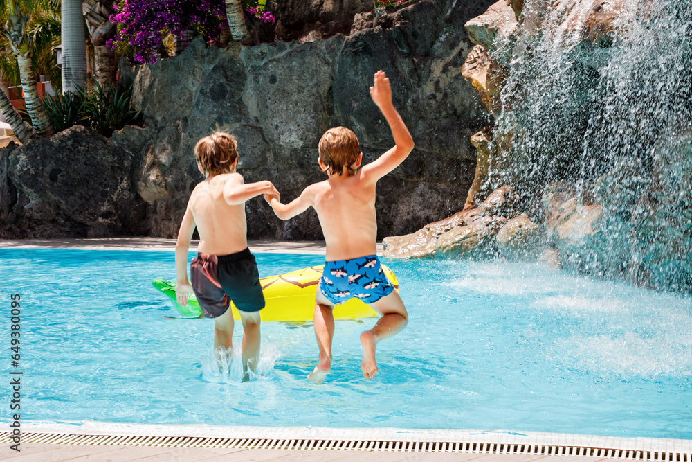 Two happy little kids boys jumping in the pool and having fun on family vacations in a hotel resort. Healthy children, siblings and best friends playing in water