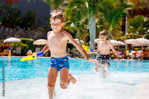 Two happy little kid boys jumping in the pool and having fun on family vacations in a hotel resort. Children playing in water with a water gun. Laughing running siblings brothers and best friends photo