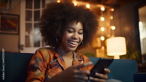 Happy relaxed gen z African American teen sitting on couch at home holding cellphone, using mobile apps on cell phone in modern living room. Social media influence concept