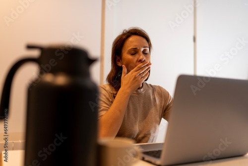 40 year old woman yawning tired at home or office with laptop. work late at the office