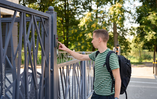 Young male at entrance door on a building ringing doorbell and talking on speaker phone. Man ringing video intercom on the gate at the entrance. photo