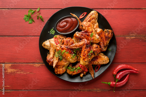Chicken wings. Grilled or baked chicken wings with sesame seeds and ketchup or spicy tomato sauce on black plate on old wooden red table background. Top view with copy space. © kasia2003