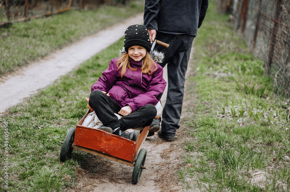 A strong man, father, grandfather rides, carries on a rusty old cart, wagon along the road in the village, countryside, a small beautiful smiling, happy girl, child. Photography, close-up portrait. A strong man, father, grandfather rides, carries on a rusty old cart, wagon along the road in the village, countryside, a small beautiful smiling, happy girl, child. Photography, close-up portrait.
