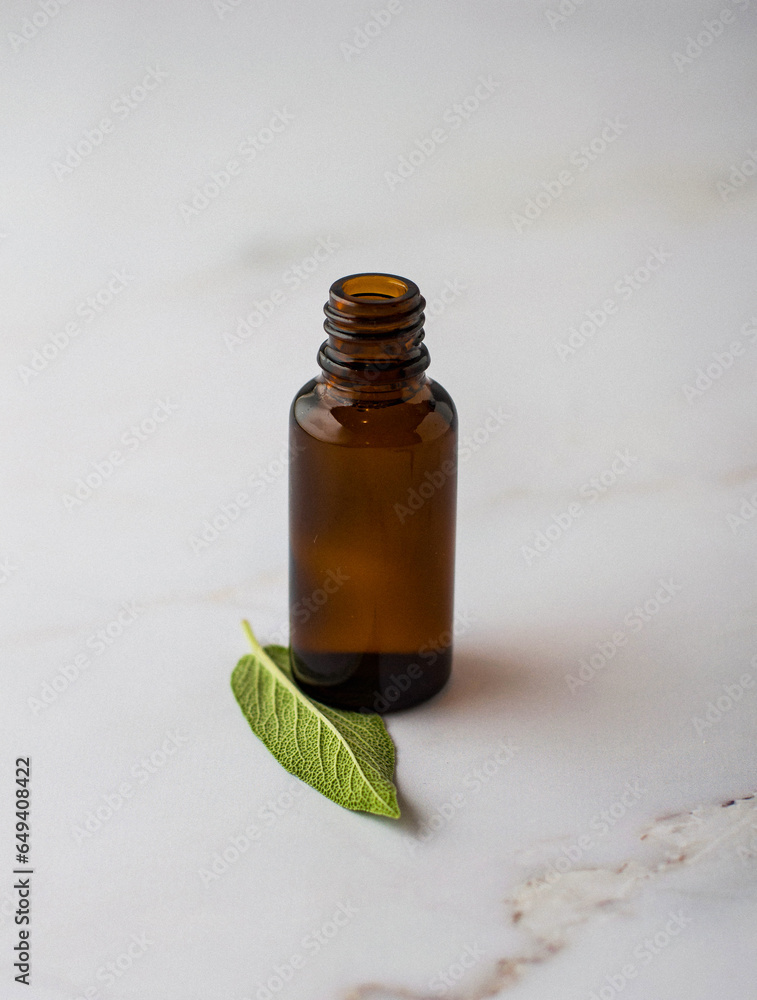 A small dark glass bottle for pharmaceuticals, medicines, solutions, aromatic oils next to sage leaves, on a light background..